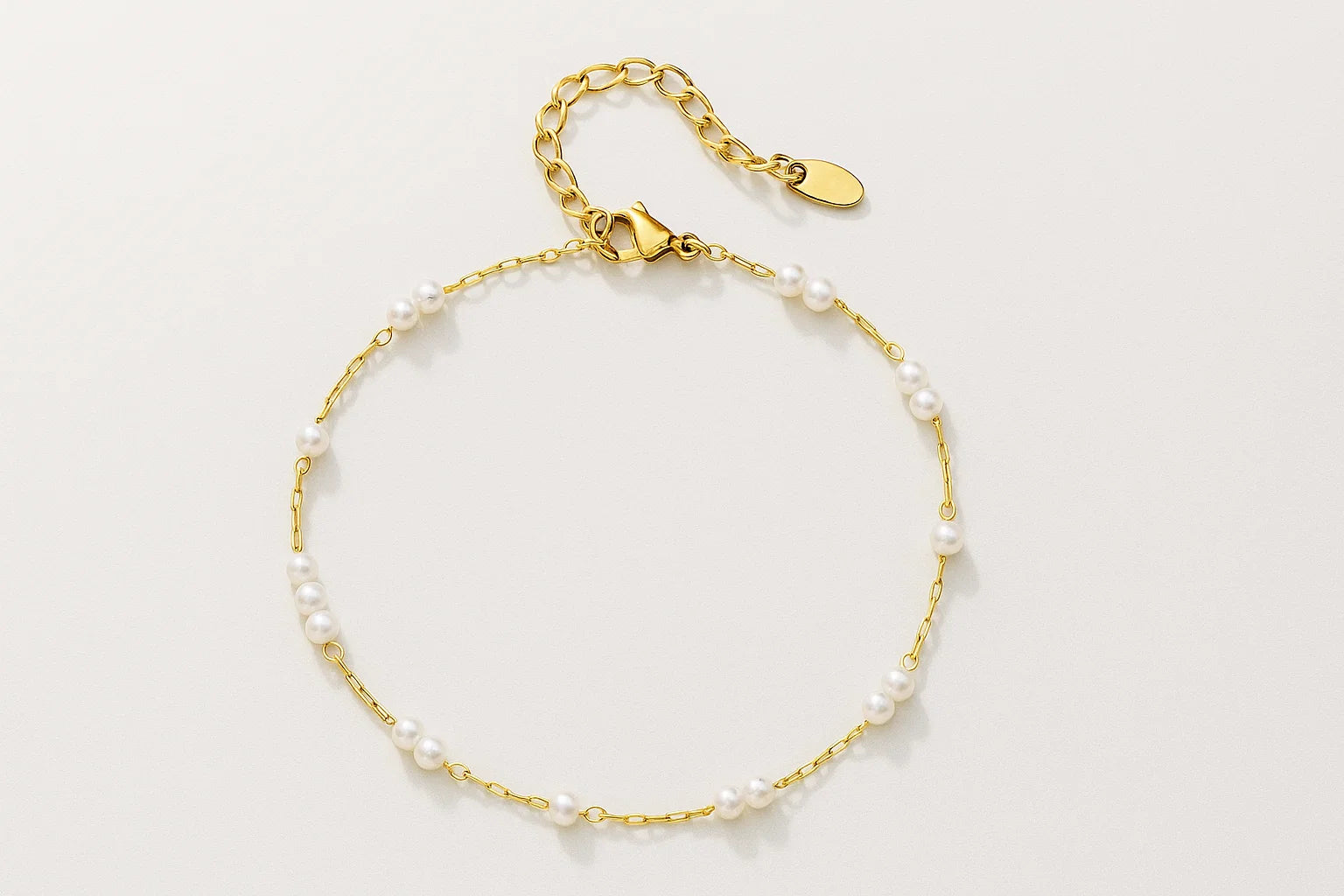 Gold bracelet with pearl beads on a light gray background